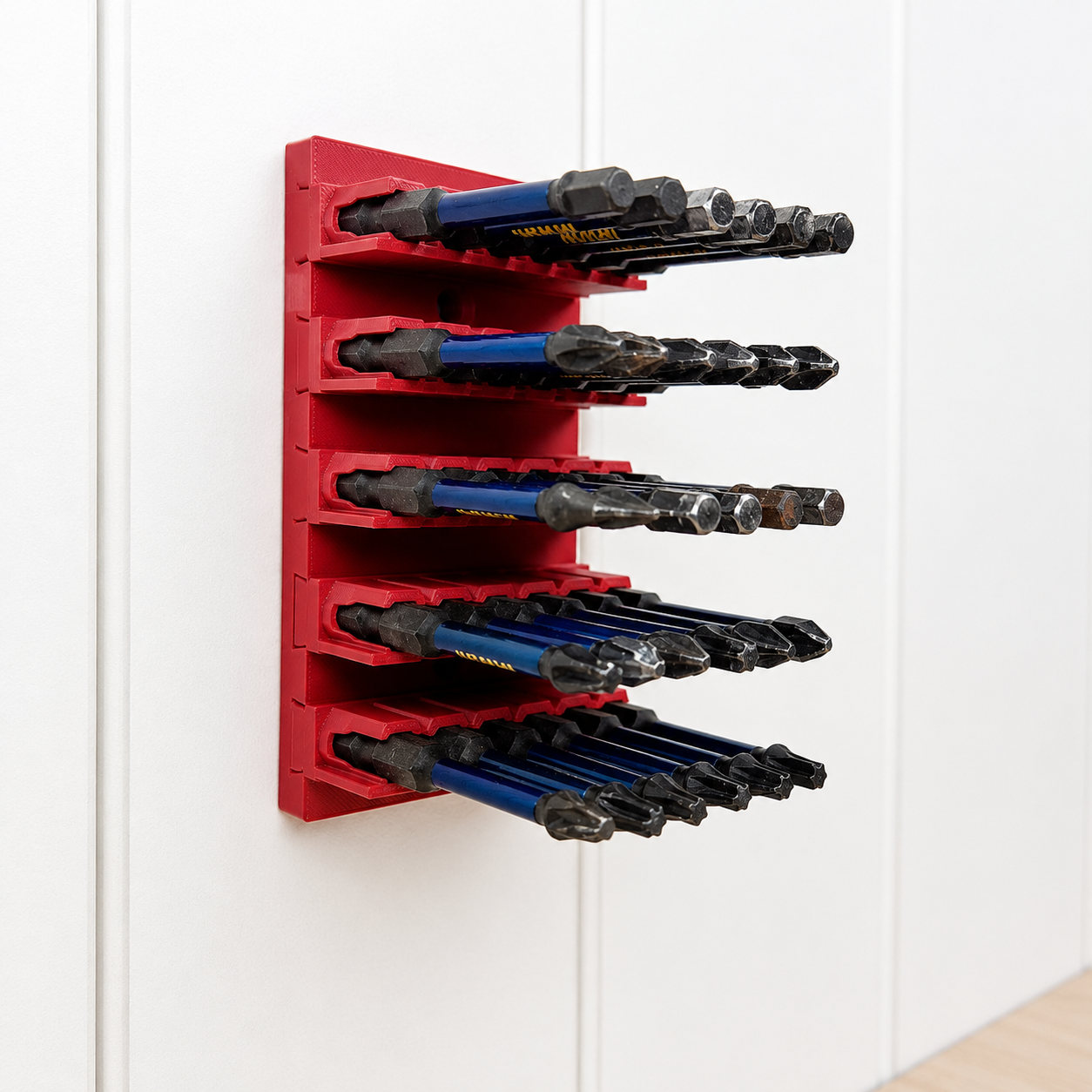 Red tool organizer bit holder holding various drill bits on a white wall.